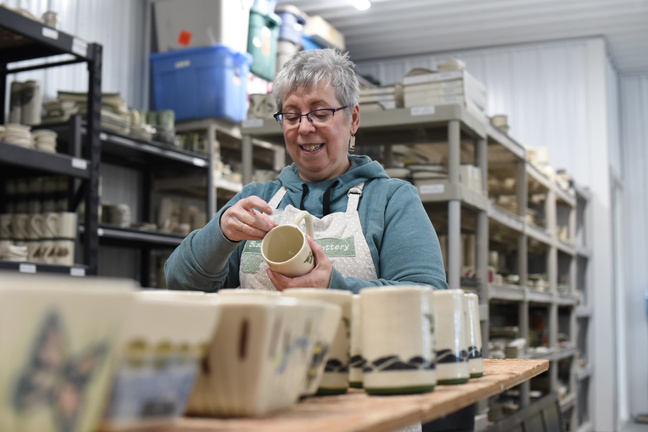 A woman inspecting handmade pottery and placing stickers on a mug
